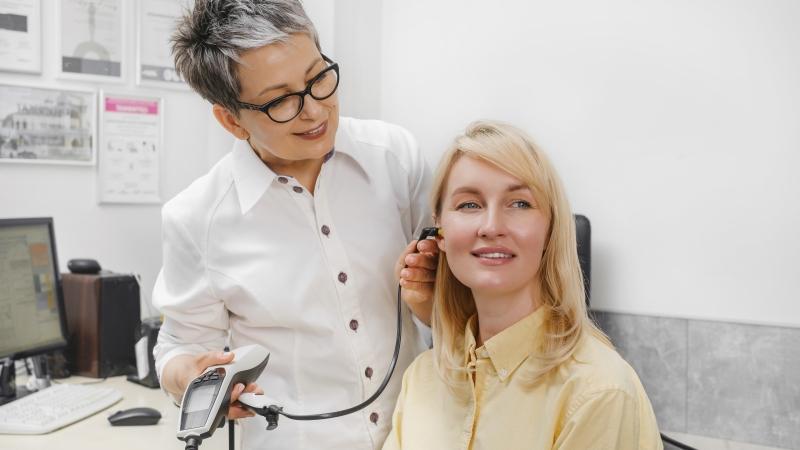 Doctor examining a woman's ear with a testing device in a doctor's office